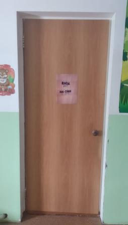На двери групповой комнаты имеется вывеска с надписью "Вход на себя", выполненной рельефно-точеным шрифтом Брайля.